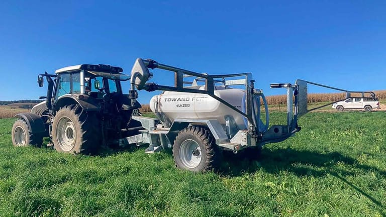 A black tractor with a Tow and Fert Multi 2800 sprayer attached, positioned in a lush green field.