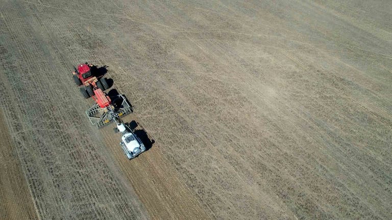 Aerial view of a red tractor towing a Tow and Fert MultiCrop 4000 sprayer across a harvested field.